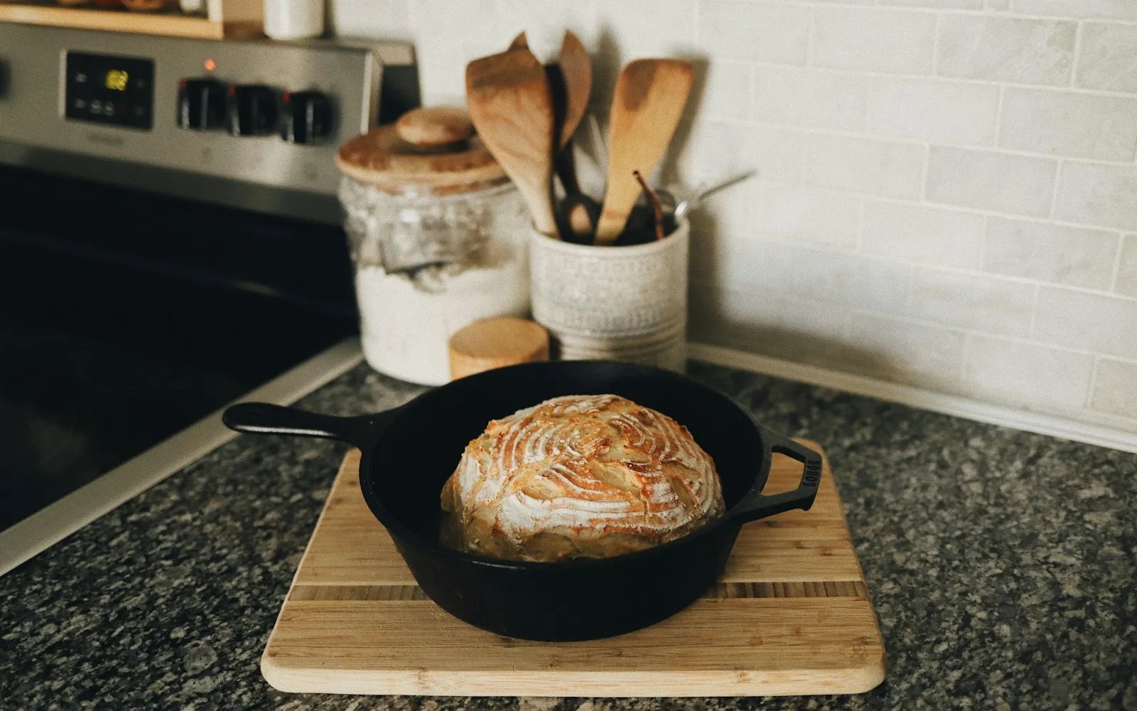Een gietijzeren pan met een vers brood op een houten plank, met houten lepels erachter