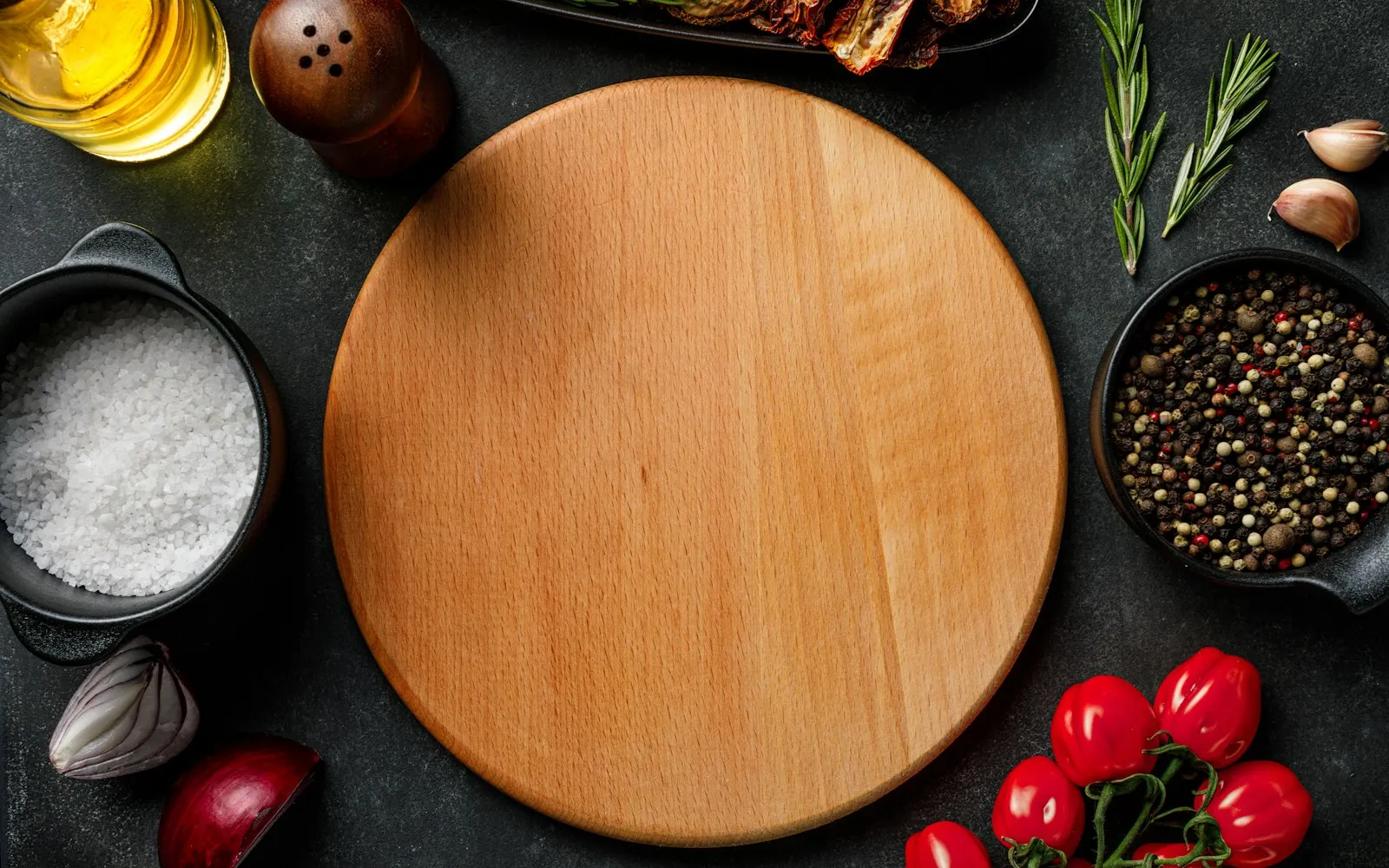 Een ronde houten snijplank tussen tomaatjes, peper, zout en kruiden